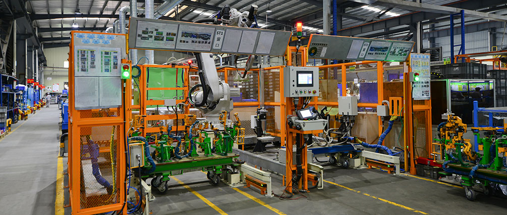 Automated automotive line with orange guarding and green equipment.