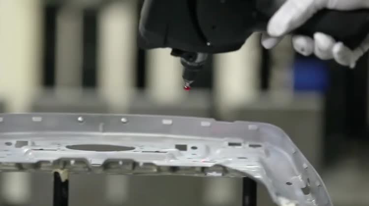 Close-up video frame of inspection probe measuring a stamped metal component.